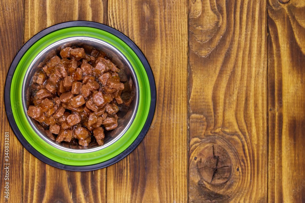 Canned food for cats or dogs in green metal bowl on wooden floor. Top view
