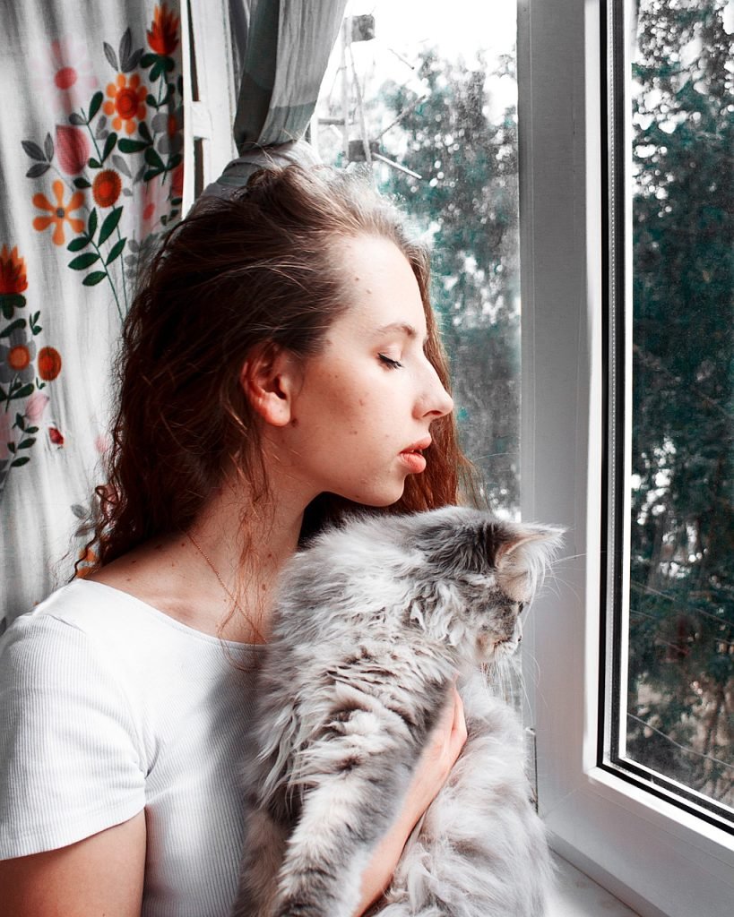 Woman holding her cat near a window at home